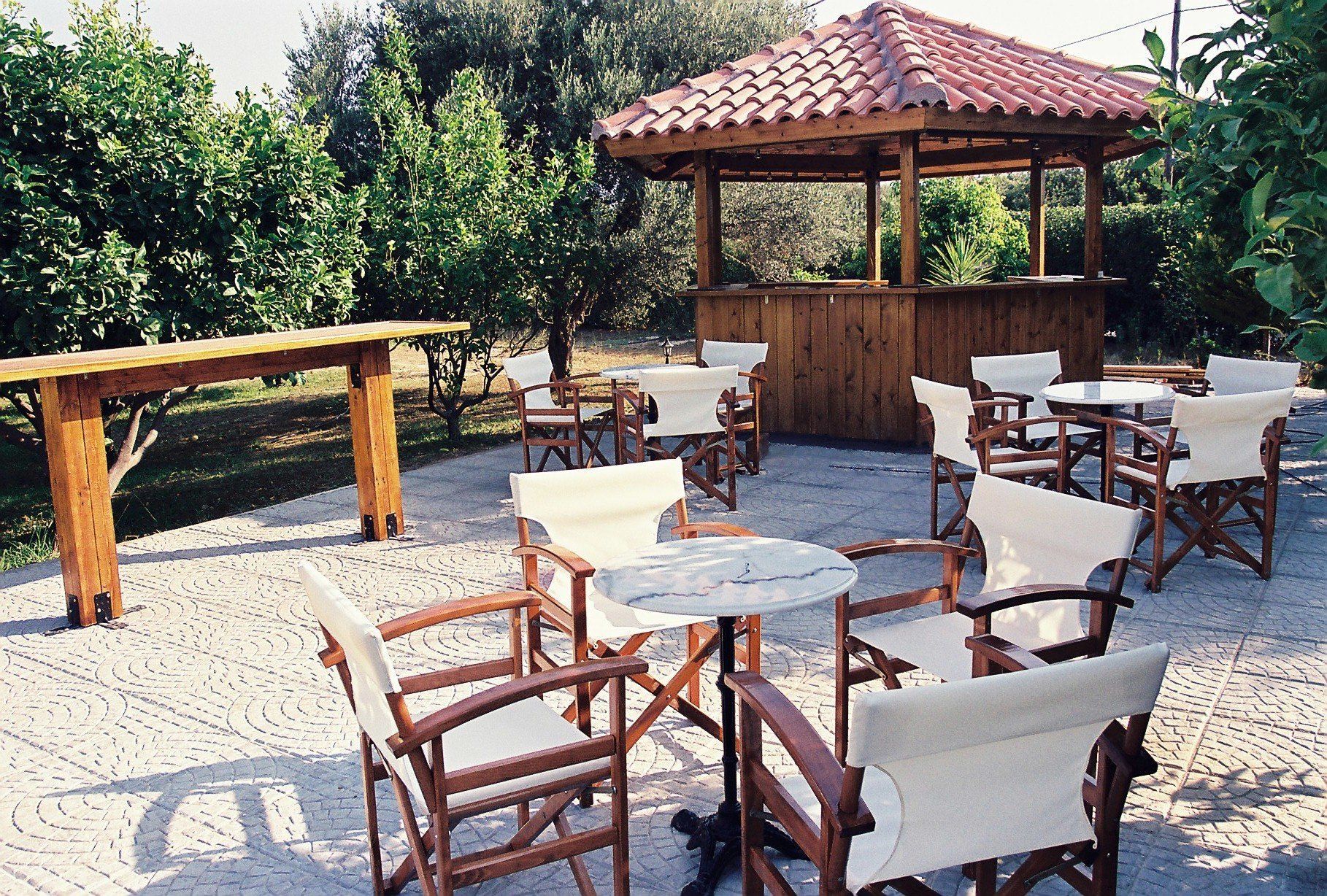 Une terrasse extérieure avec des tables et des chaises en bois, un gazebo en bois et une zone dallée.