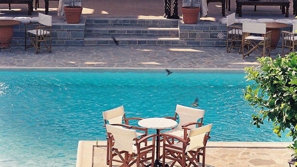 A poolside area with outdoor seating, a stone archway, and a view of the pool. - Nicolas Village Club (Aigialeia)
