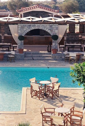 A poolside area with outdoor seating, a stone archway, and a view of the pool. - Nicolas Village Club (Aigialeia)
