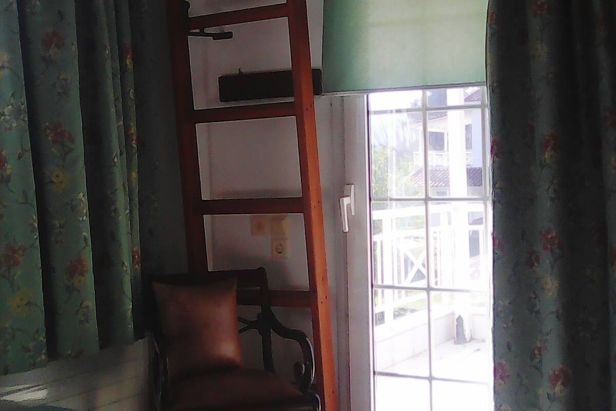A room with a bed, a chair, a ladder, and a window with curtains.