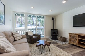 Ein modernes Wohnzimmer mit einem beigefarbenen Sofa, einem braunen Ledersessel, einem Holztisch, einem an der Wand montierten Fernseher und einem Kamin.