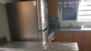 Una cocina con encimera de granito, refrigerador de acero inoxidable, taburetes de madera y armarios de madera.