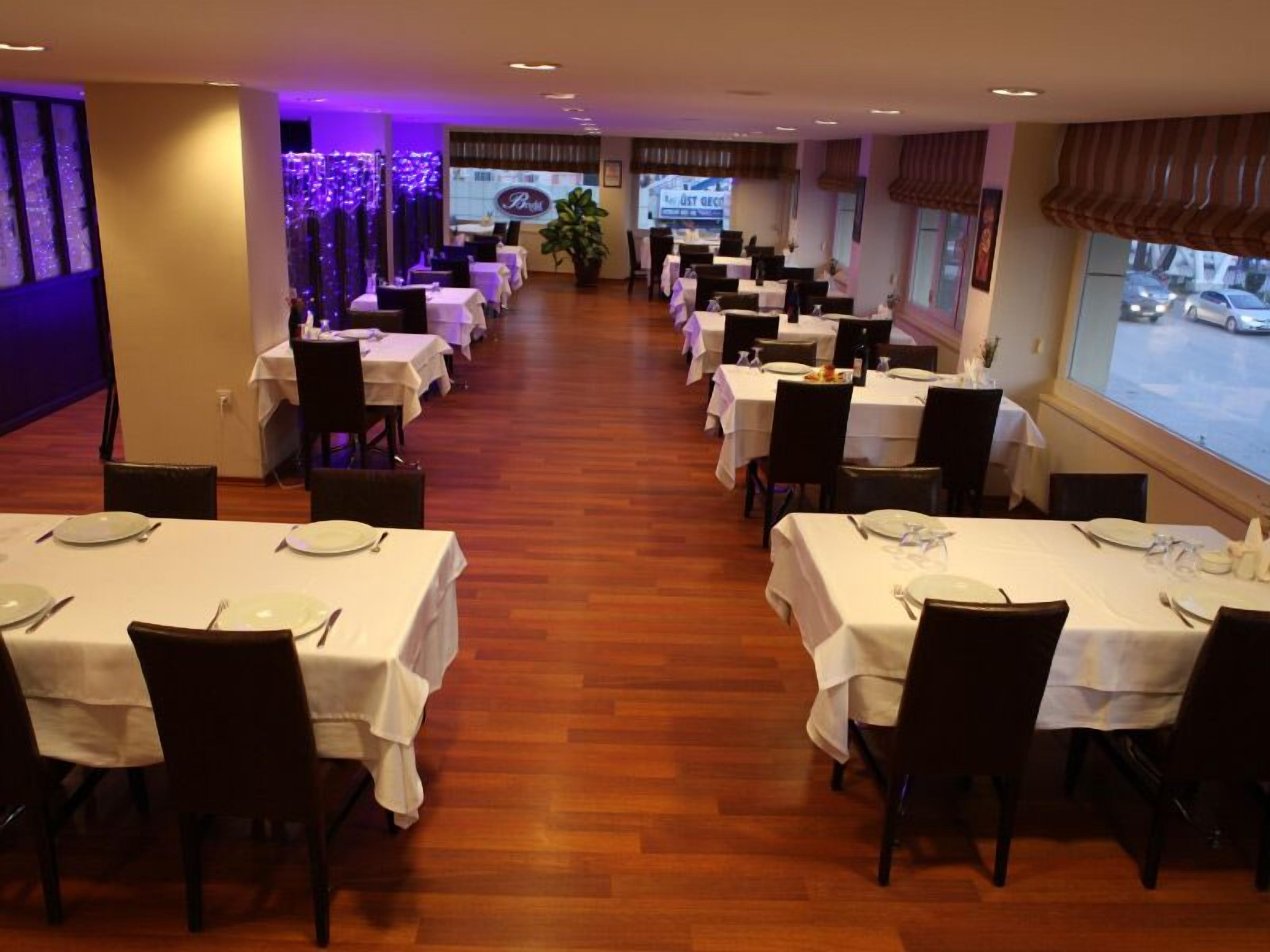Un restaurante con varias mesas preparadas para comer, suelo de madera y vista a la calle a través de amplios ventanales.