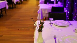 Un restaurante con mesas preparadas para comer, una pantalla de televisión al fondo y una iluminación ambiental morada.