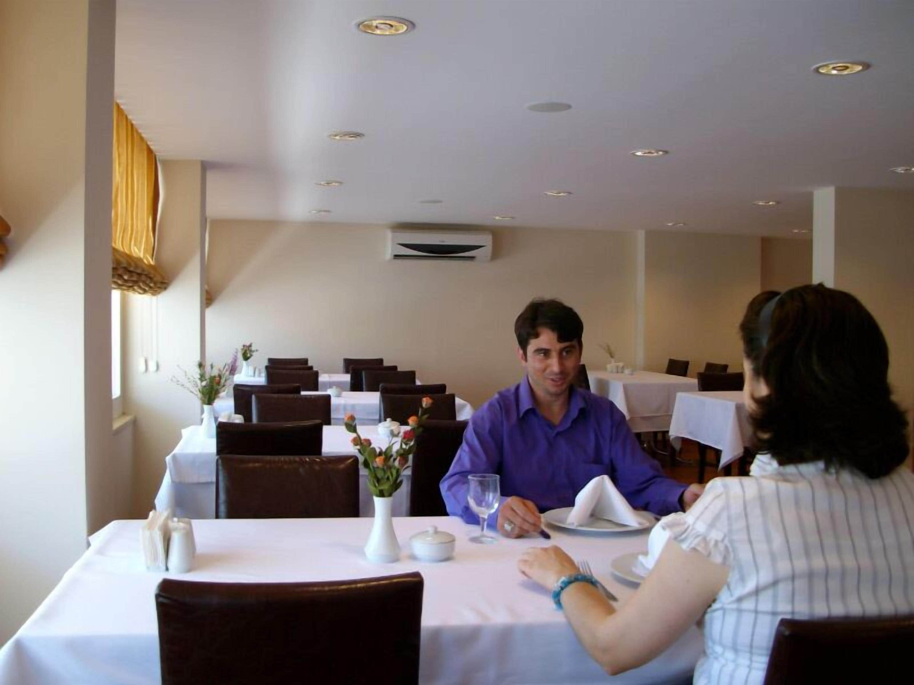 Un restaurante con mesas preparadas para dos, manteles blancos y un jarrón con flores en cada una.