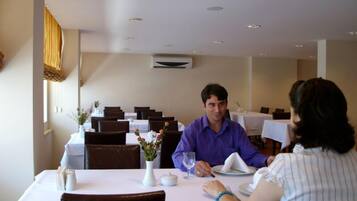 Un restaurante con mesas preparadas para dos, manteles blancos y un jarrón con flores en cada una.