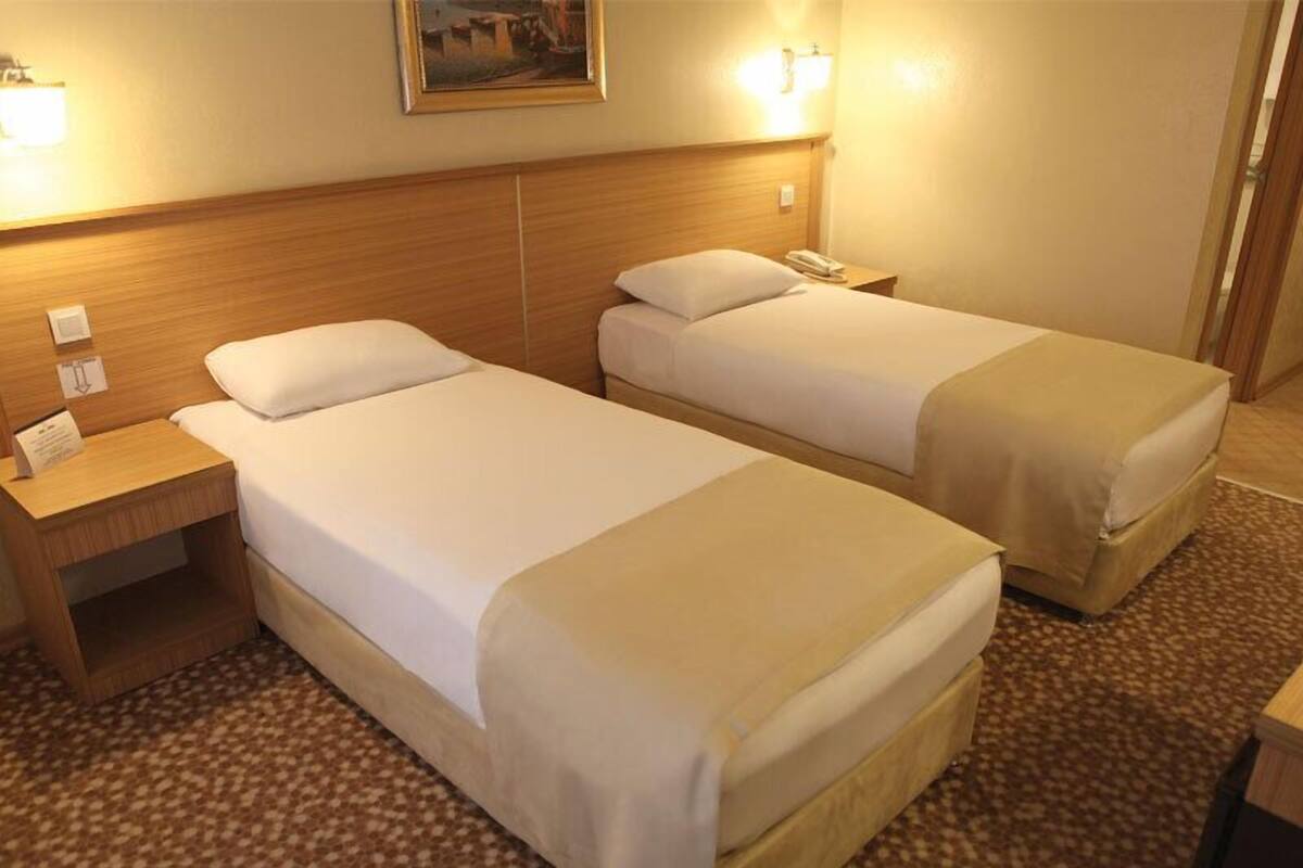 A hotel room with two single beds, a wooden headboard, bedside tables, and a carpeted floor.