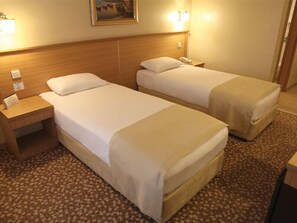 A hotel room with two single beds, a wooden headboard, bedside tables, and a carpeted floor.