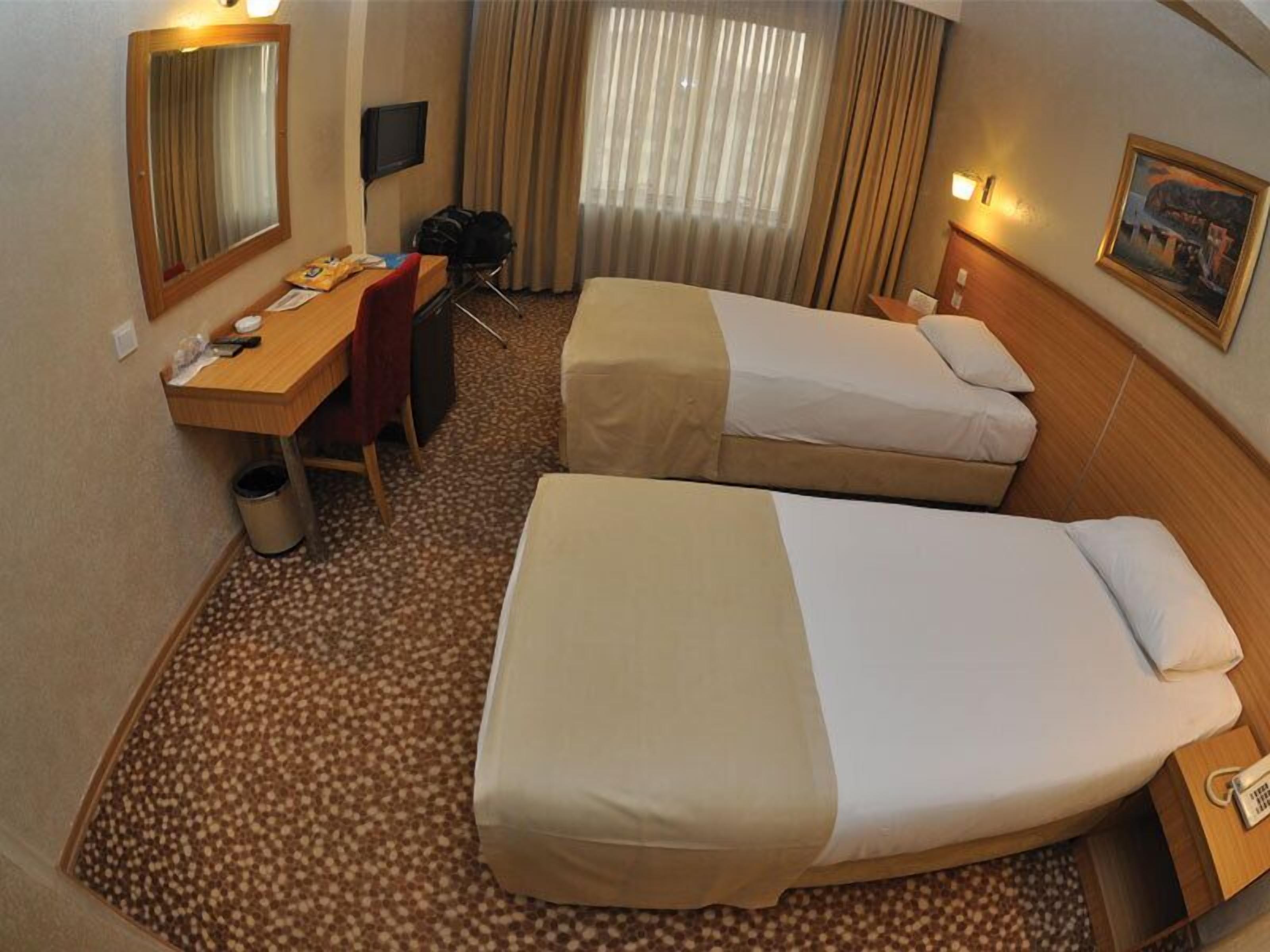 Een hotelkamer met twee enkele bedden, een bureau met stoel, een klein tafeltje, een prullenbak en een televisie.