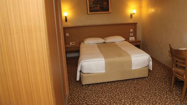 Una habitación de hotel con una cama, dos lámparas de noche, una mesita de noche, una silla y suelo alfombrado.
