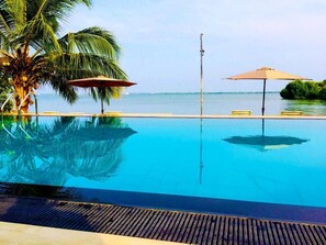 Ein klares, blaues Schwimmbecken mit Palmen und Sonnenschirmen, umgeben von einer Holzterrasse.
