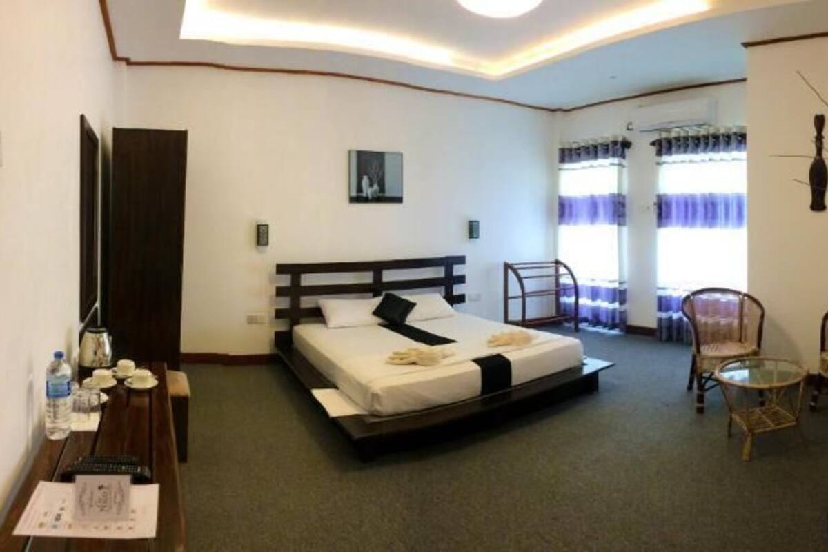 A hotel room with two beds, a desk with a chair, a small table, and a window with curtains.