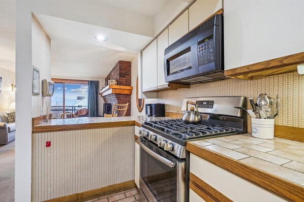 A kitchen with a gas stove, oven, microwave, and a coffee maker. There is a wooden countertop and a brick wall. - Ski-in/ski-out 2 bedroom Sunrise Village condo with pool and hot tub. (Killington)
