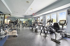 A gym with various exercise machines, large windows, and a mirrored wall.