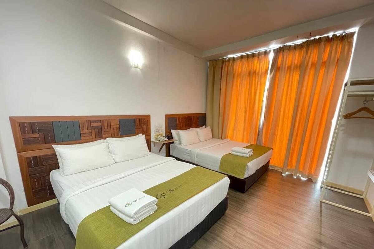 Habitación de hotel con dos camas, cabeceros de madera, suelo de madera y una ventana con cortinas naranjas.