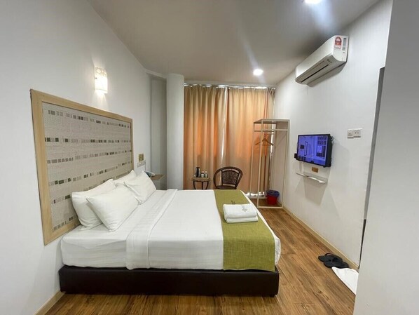 A hotel room with a bed, a TV, an air conditioner, and a window with curtains.