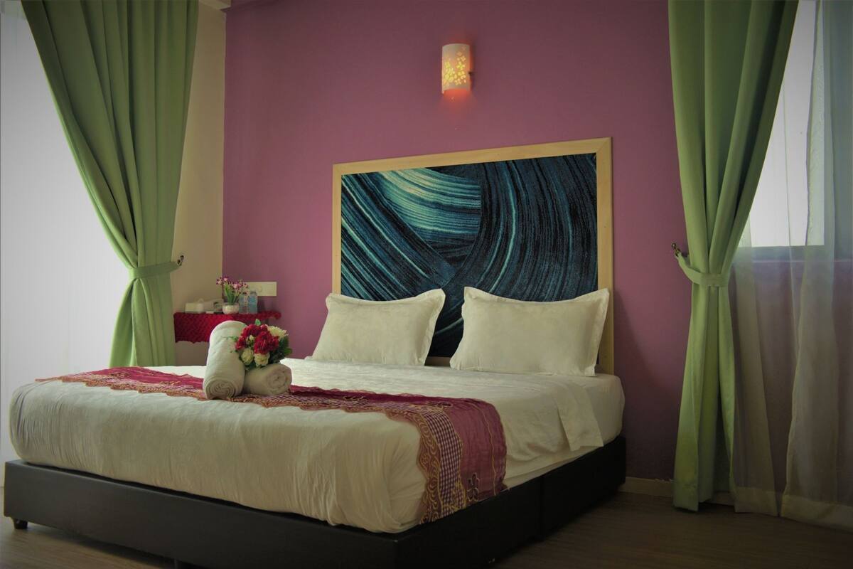 Una cama con sábanas blancas, un cabecero con un cuadro abstracto azul y cortinas verdes.