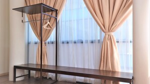 Una habitación con un banco de madera, un estante metálico con perchas y cortinas translúcidas.