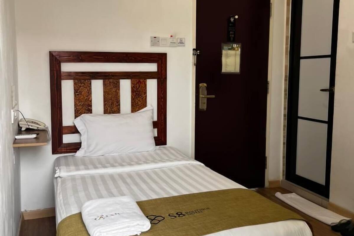 Una habitación de hotel con una cama, una mesita de noche con teléfono, una lámpara de pared y una puerta con espejo.