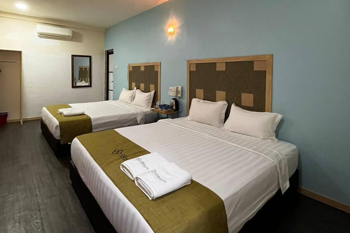 Habitación de hotel con dos camas, una mesita de noche, un teléfono en la pared y una pequeña mesa con una lámpara.