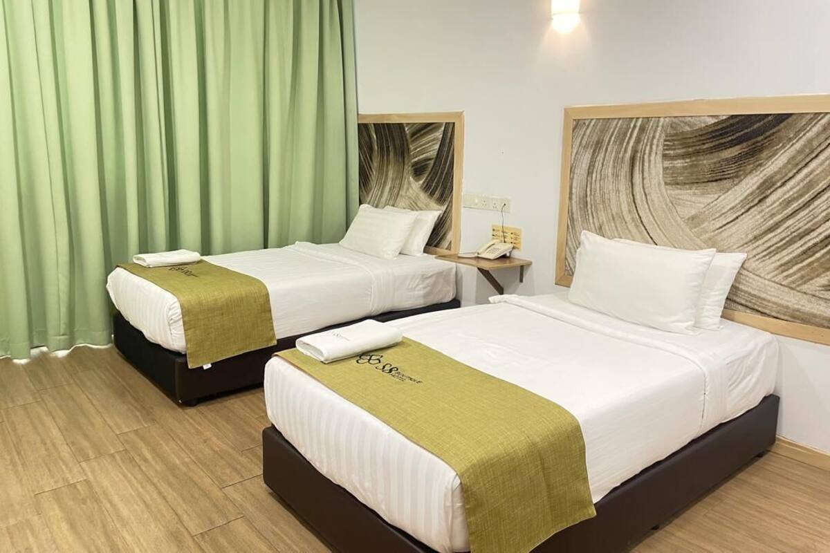 Dos camas individuales con cabeceros de madera, una cortina verde, una mesita de noche con teléfono, y una lámpara de pared.