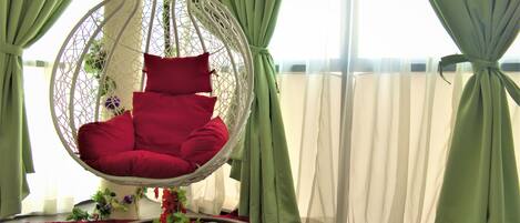 Una habitación con una silla colgante, cortinas verdes y una alfombra roja.