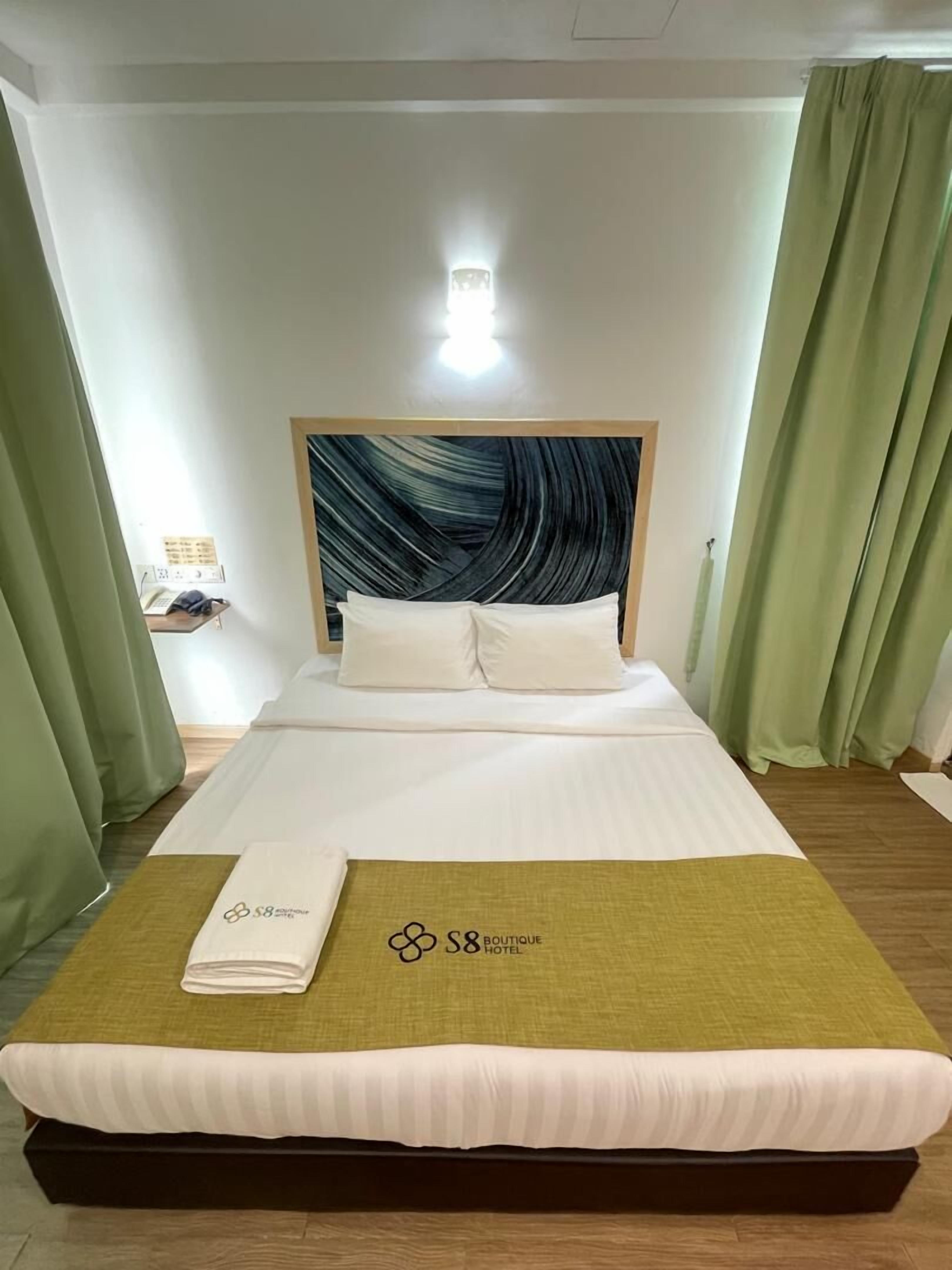 Habitación de hotel con una cama, cabecera con diseño de olas, luz nocturna y cortinas verdes.