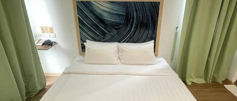Habitación de hotel con una cama, cabecera con diseño de olas, luz nocturna y cortinas verdes.