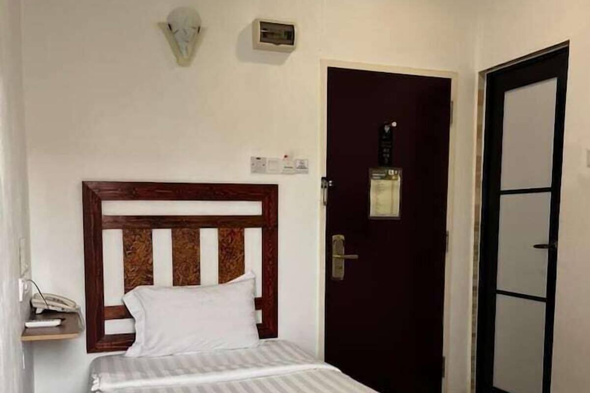 Habitación de hotel con cama, mesita de noche, luz empotrada en la pared, puerta y espejo.