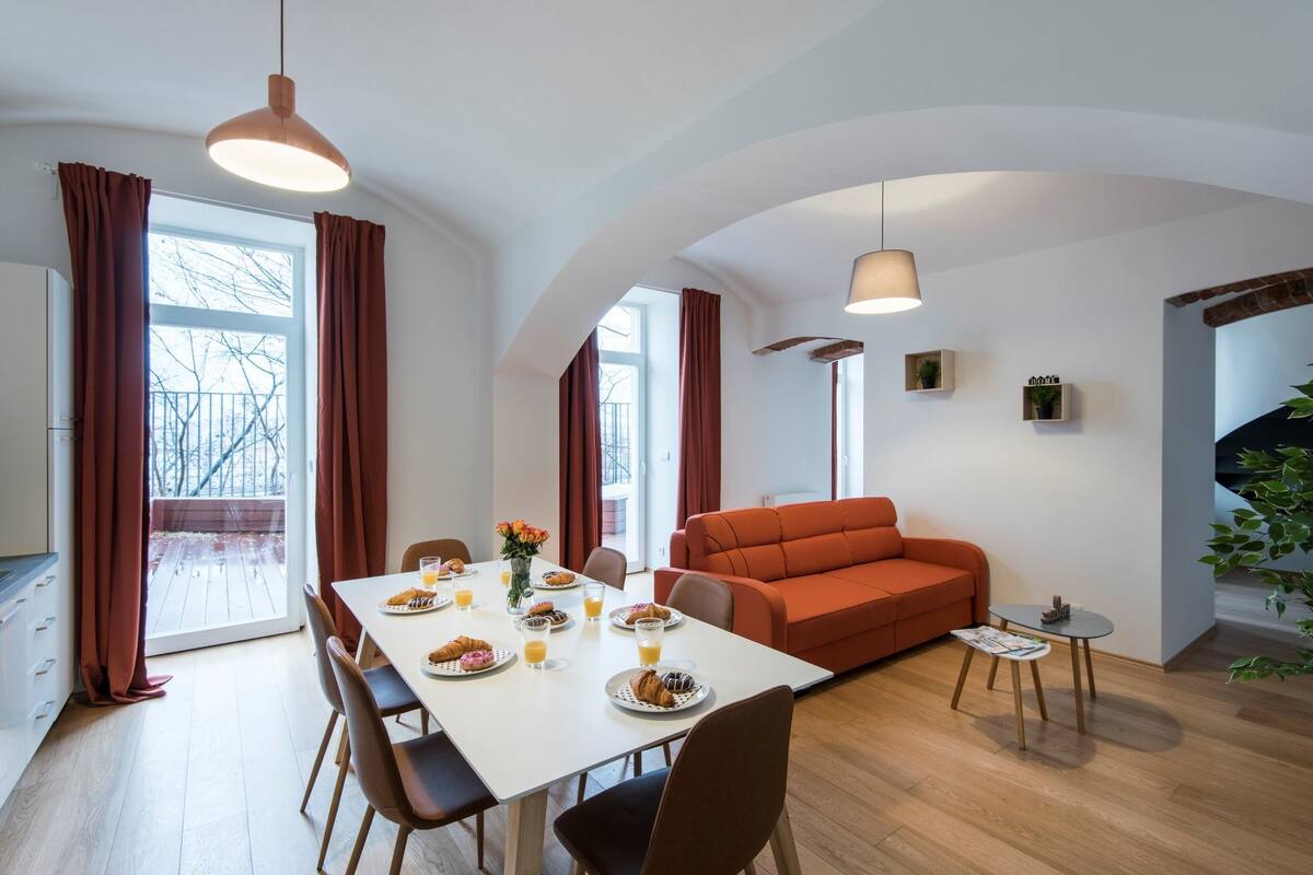 Uma zona de refeições moderna com uma mesa branca posta para o pequeno-almoço, um sofá vermelho e uma pequena mesa lateral.