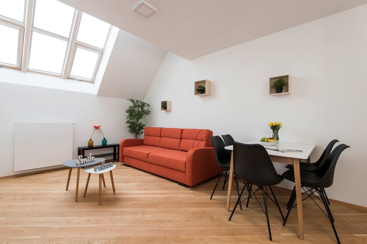 Uma sala de estar moderna com um sofá vermelho, uma mesa de jantar com quatro cadeiras e um claraboia acima.