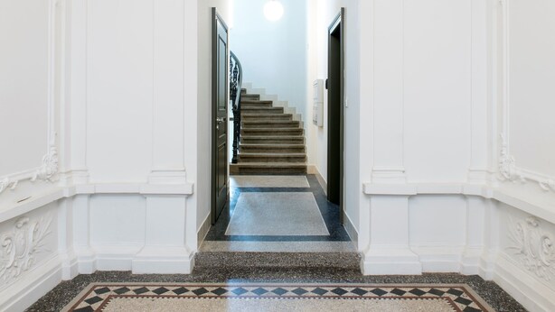 Un vestíbulo imponente con una escalera de mármol, paredes blancas y molduras decorativas.