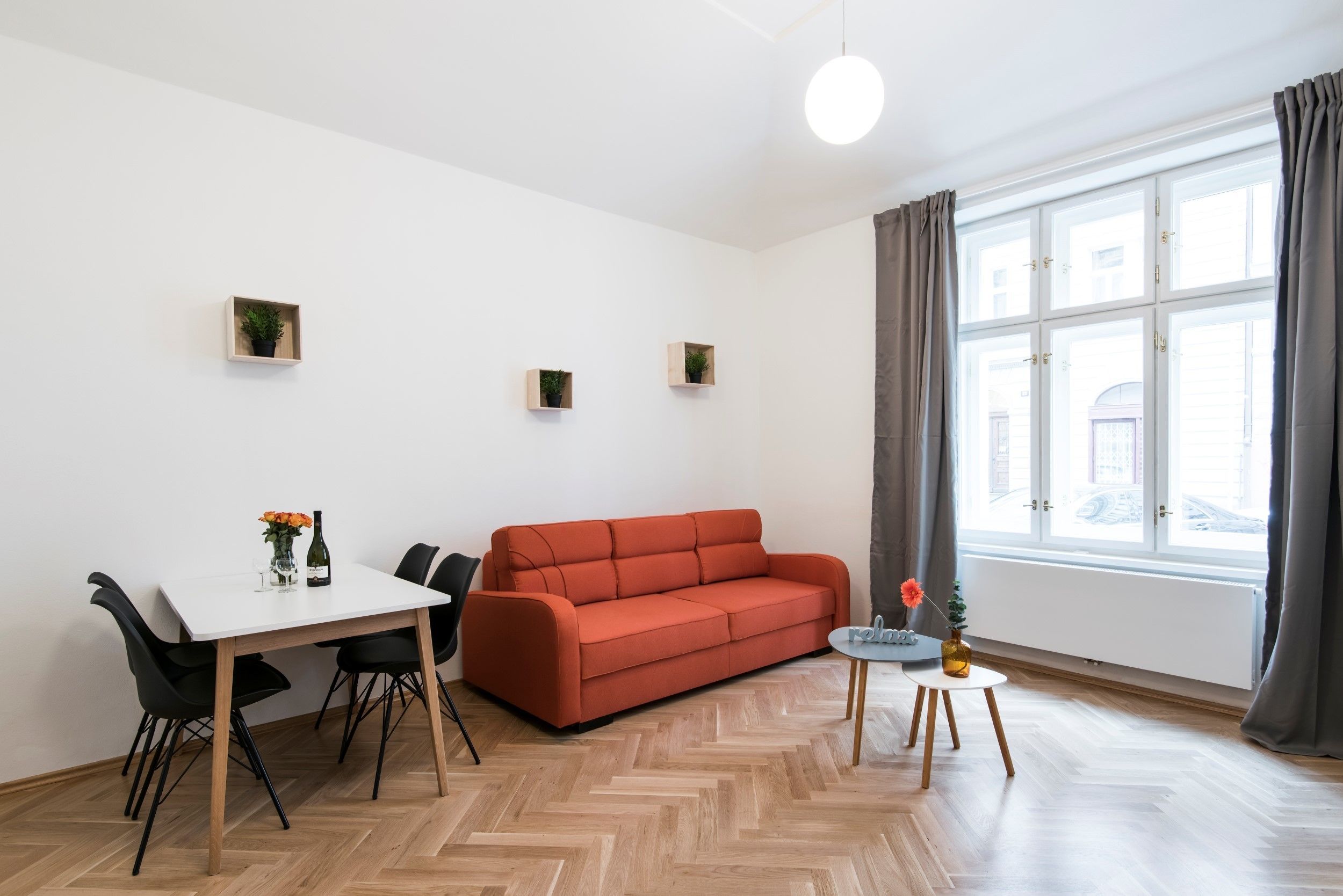 A modern living room with a white table, red sofa, and a small side table with a vase.