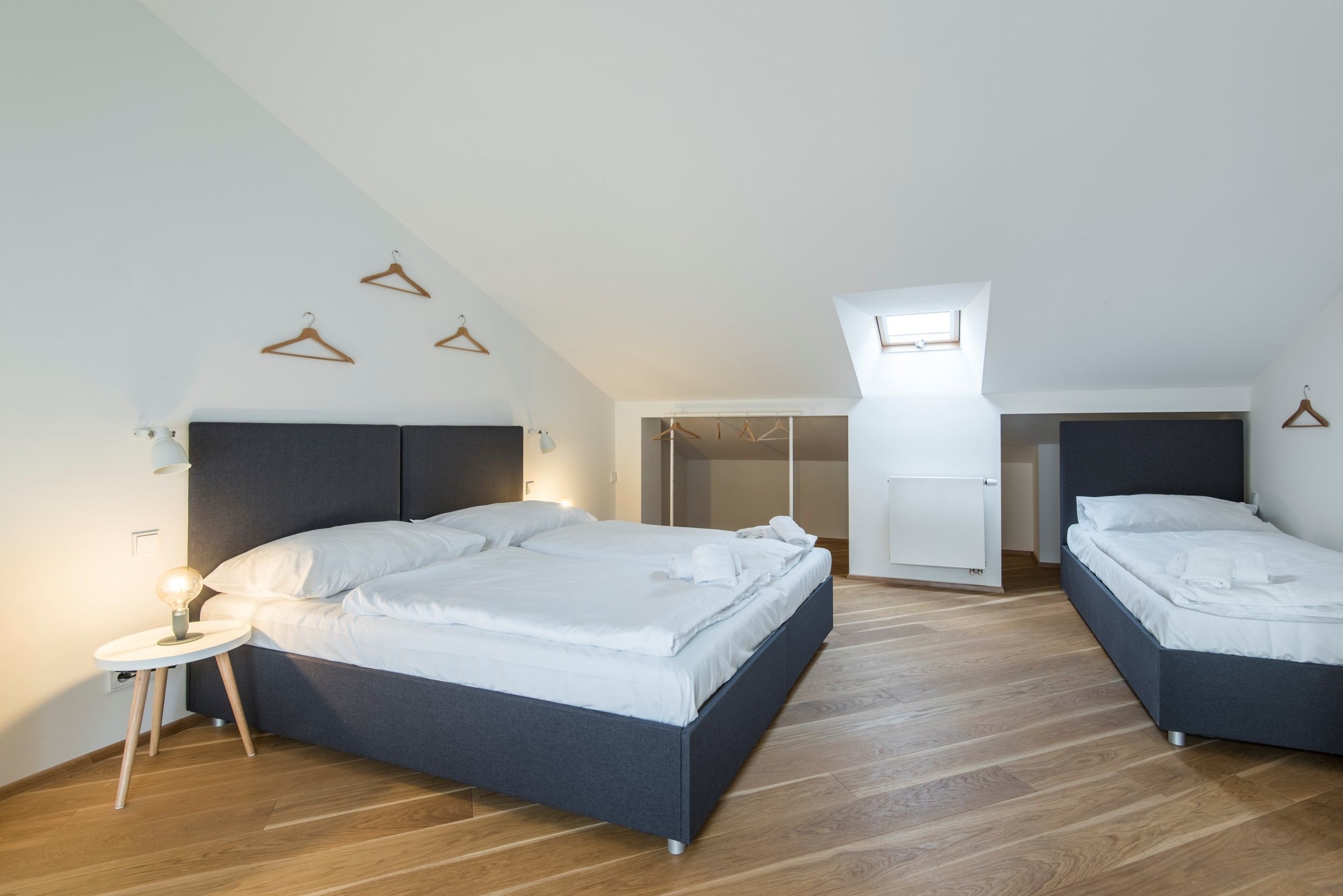 A modern bedroom with a large bed, two smaller beds, a walk-in closet, and a skylight.