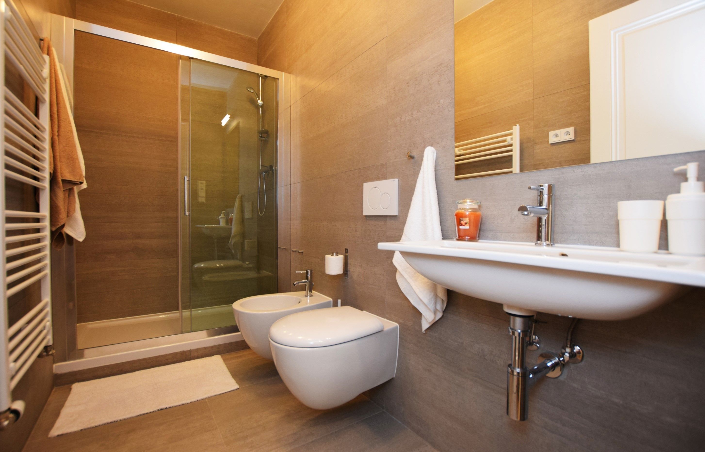 A modern bathroom with a glass shower enclosure, a bidet, a toilet, and a sink with a mirror above it.