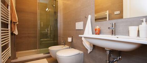 A modern bathroom with a glass shower enclosure, a bidet, a toilet, and a sink with a mirror above it.
