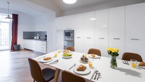 Un comedor moderno con una mesa blanca dispuesta para el desayuno, incluyendo croissants, fruta y jugo.