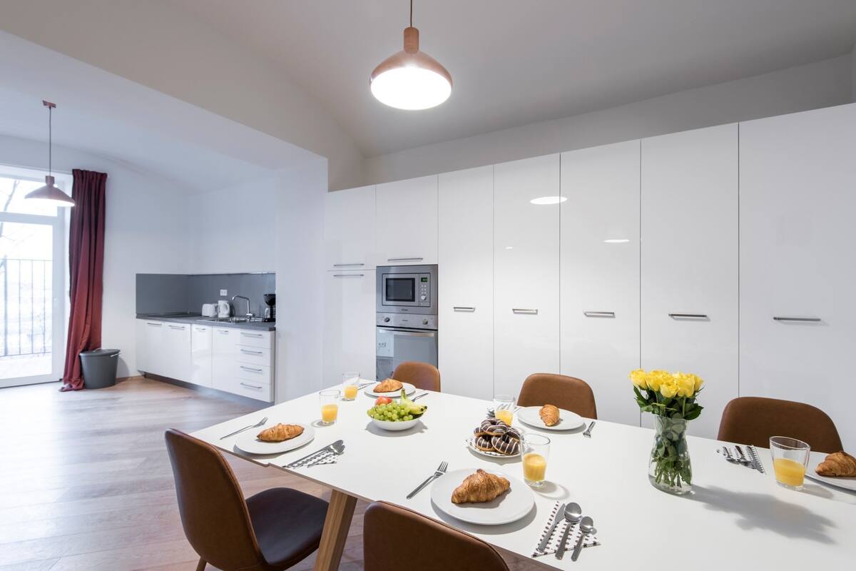 Uma sala de jantar moderna com uma mesa branca posta para o café da manhã, incluindo croissants, frutas e suco.