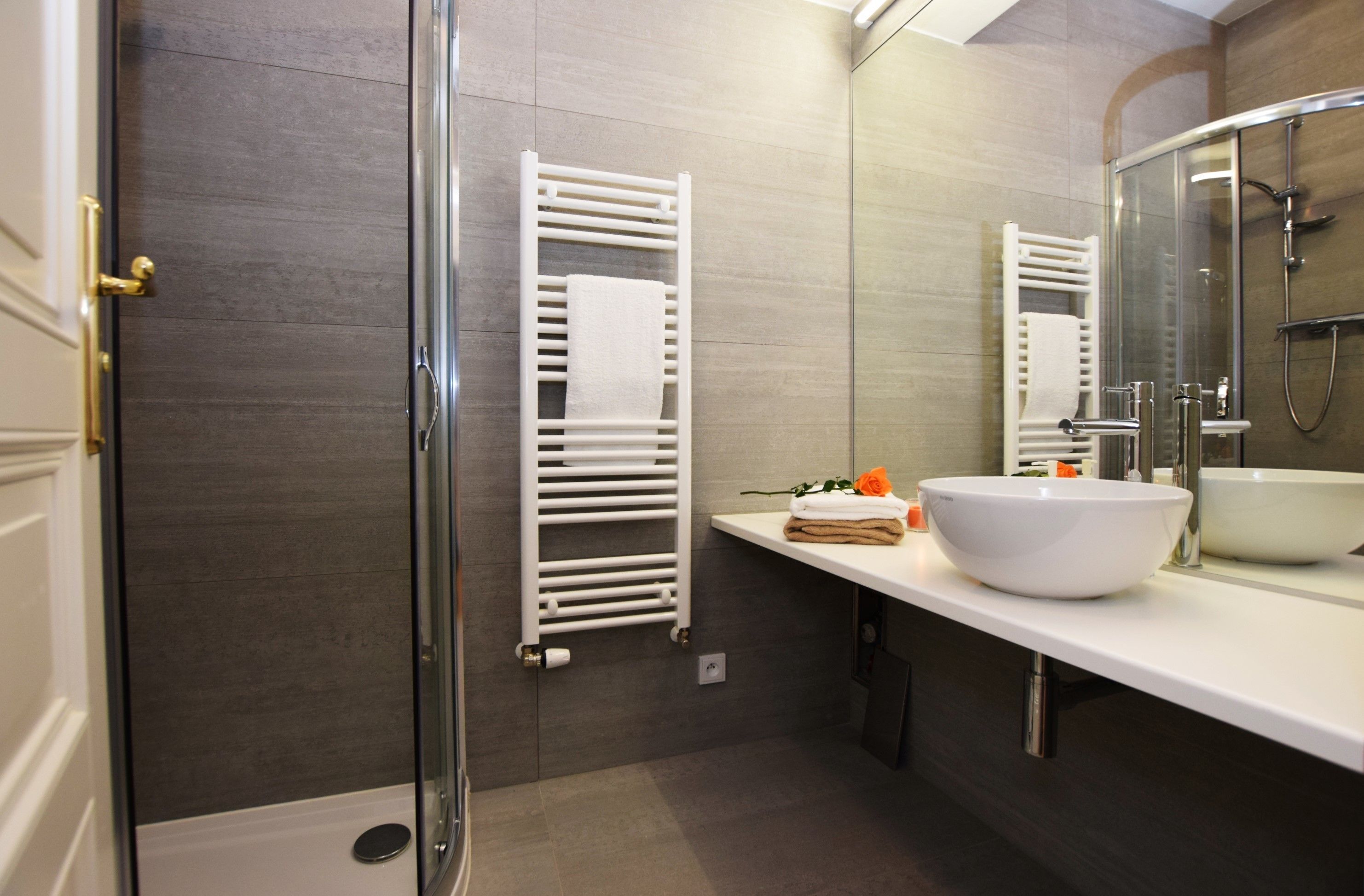 A modern bathroom with a glass shower enclosure, a white sink, and a towel rack.