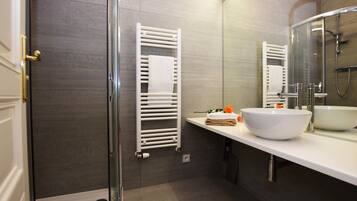 A modern bathroom with a glass shower enclosure, a white sink, and a towel rack.