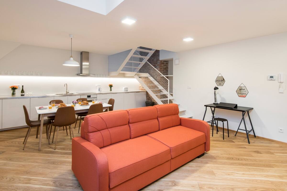 Um interior moderno com área de refeições, sofá, escada e escrivaninha.