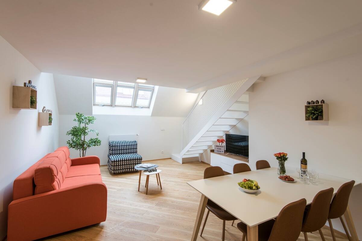 Um espaço de estar moderno com sofá, mesa de jantar para quatro pessoas, escada e uma pequena planta.