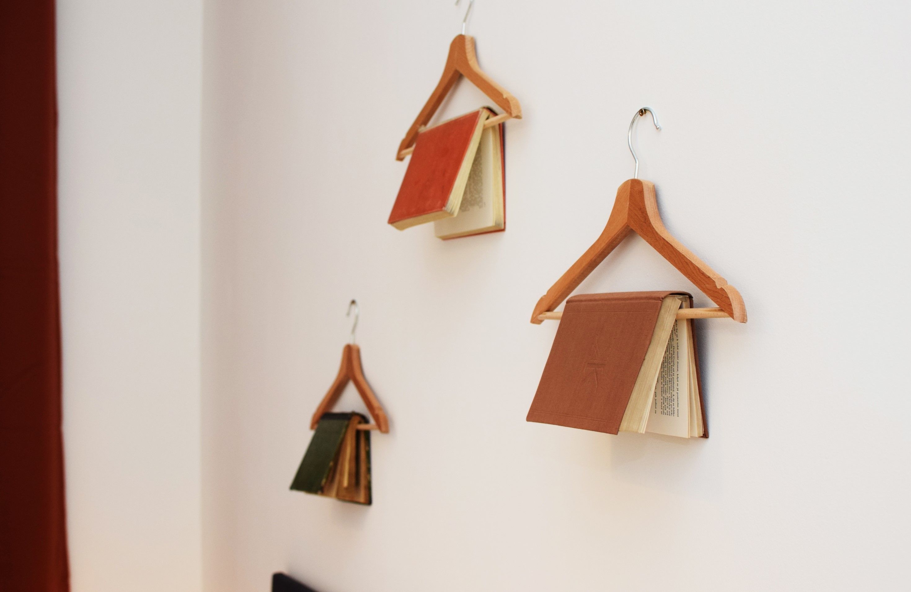 Three wooden hangers with books hanging on a white wall.