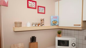 Una cocina con microondas, estante con frascos y bloque de cuchillos.
