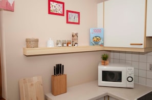 Una cocina con microondas, estante con frascos y bloque de cuchillos.