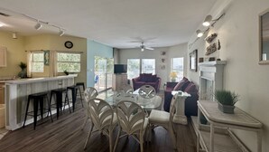 Ampla sala de estar com mesa de jantar rodeada por cadeiras, área de cozinha com balcão e espaço para relaxar com sofá e poltronas.