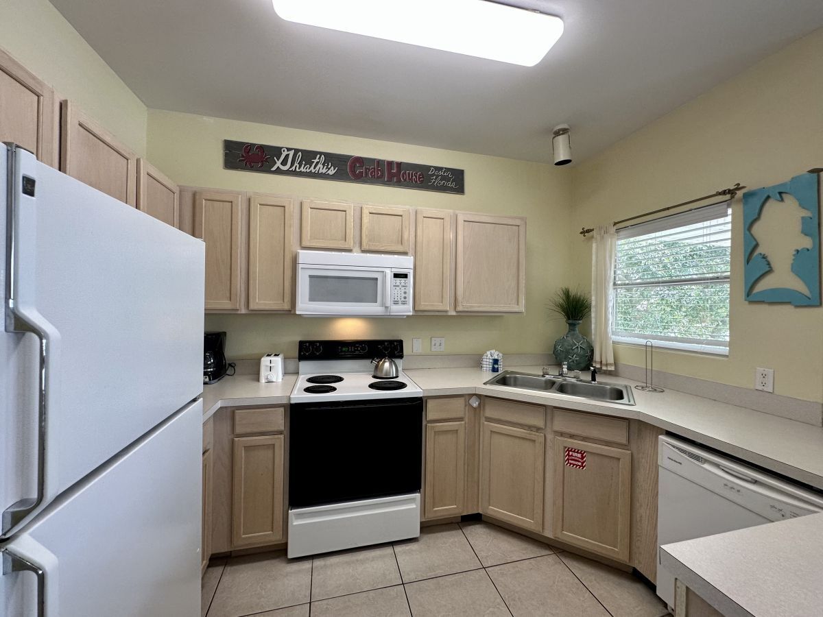 Une cuisine avec des meubles de rangement en bois, un réfrigérateur blanc, un four à micro-ondes, une cuisinière et un lave-vaisselle.