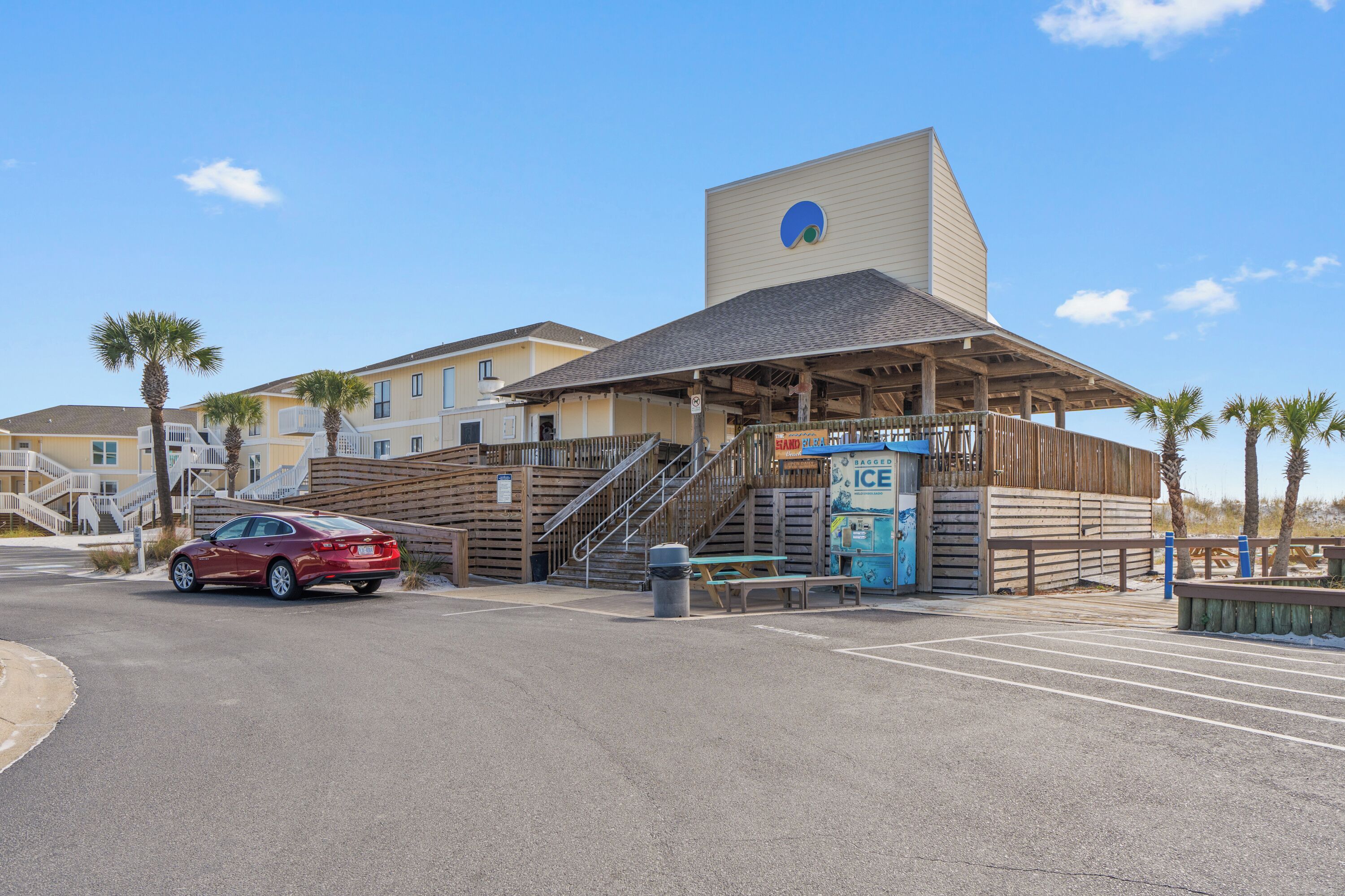A building with a large entrance, a staircase, and a parking area with a red car.