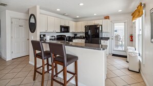A modern kitchen with white cabinets, a black refrigerator, and a granite island with two bar stools.