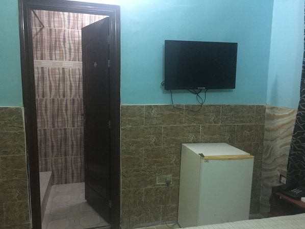 A room with a tiled wall, a television mounted on the wall, and a small white cabinet.